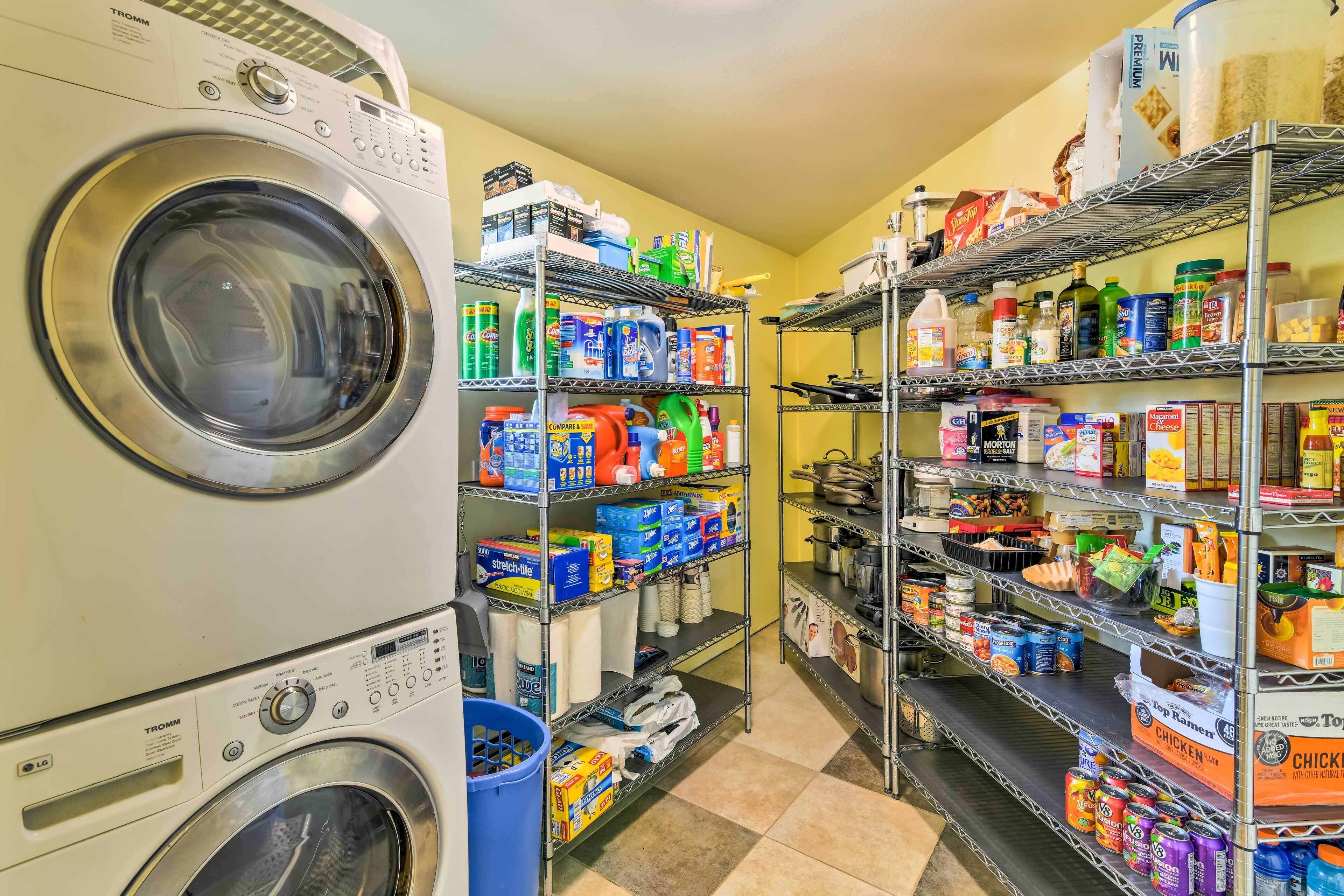 A laundry room with stacked washing machines, shelves stocked with cleaning supplies, and a variety of food items.