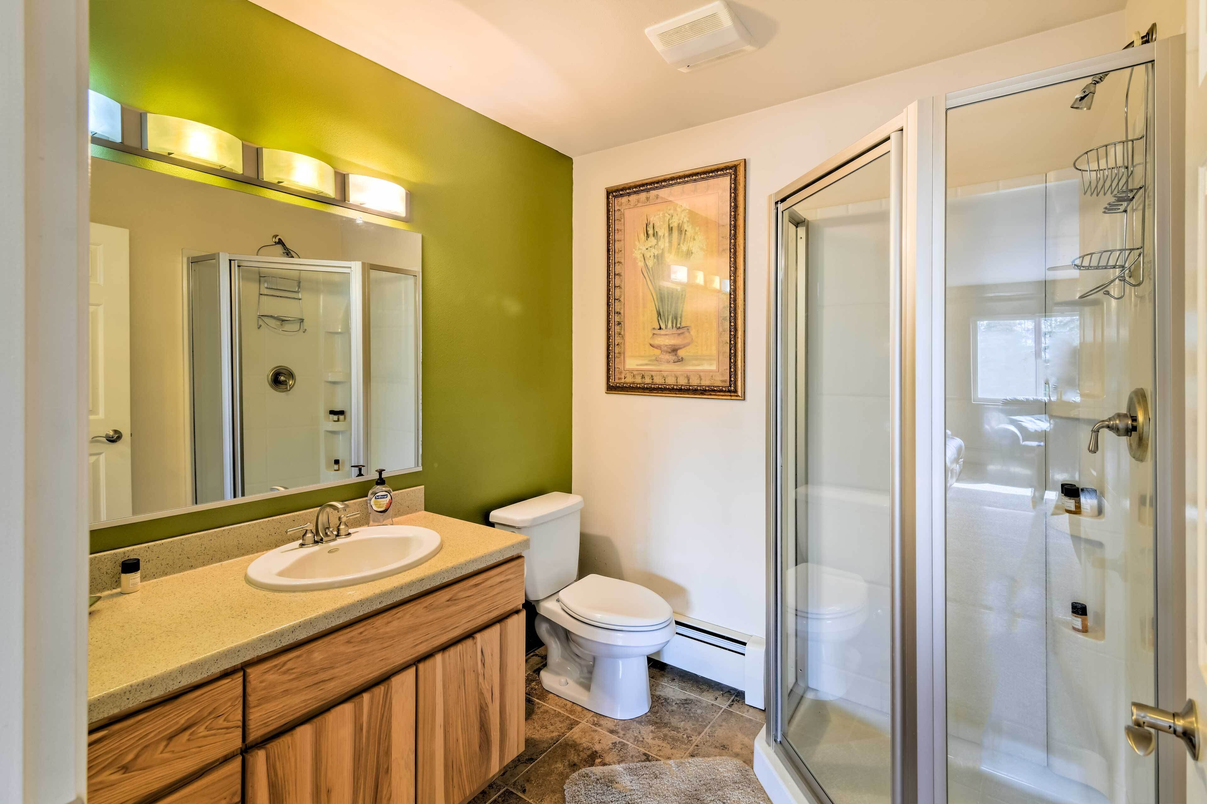 A bathroom with a wooden vanity, a white sink, a toilet, and a glass-enclosed shower.