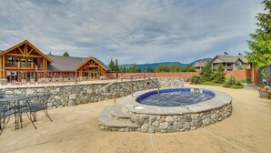 Ein Whirlpool, umgeben von Steinstufen, eine Terrasse mit Gartenmöbeln und ein Holzhaus mit großen Fenstern.