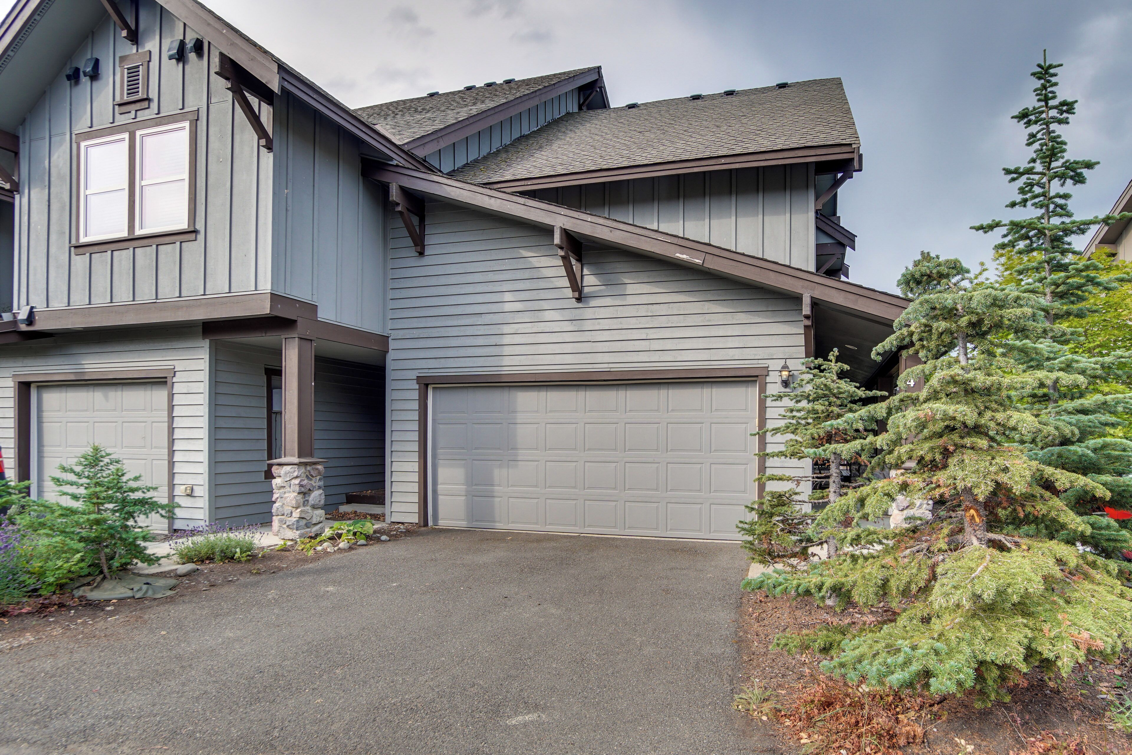 A two-story house with a garage, stone pillar, and a large evergreen tree in the driveway.