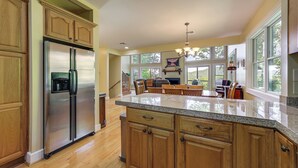 A spacious kitchen with wooden cabinets, a stainless steel refrigerator, and a large island with a granite countertop. - Mountain View Home: Hike, Raft, Golf + More! (Bryson City)