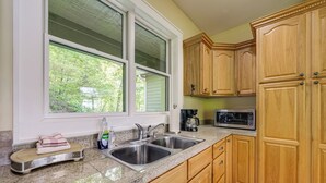 A kitchen with two sinks, wooden cabinets, a microwave, and a window with a view of trees. - Mountain View Home: Hike, Raft, Golf + More! (Bryson City)