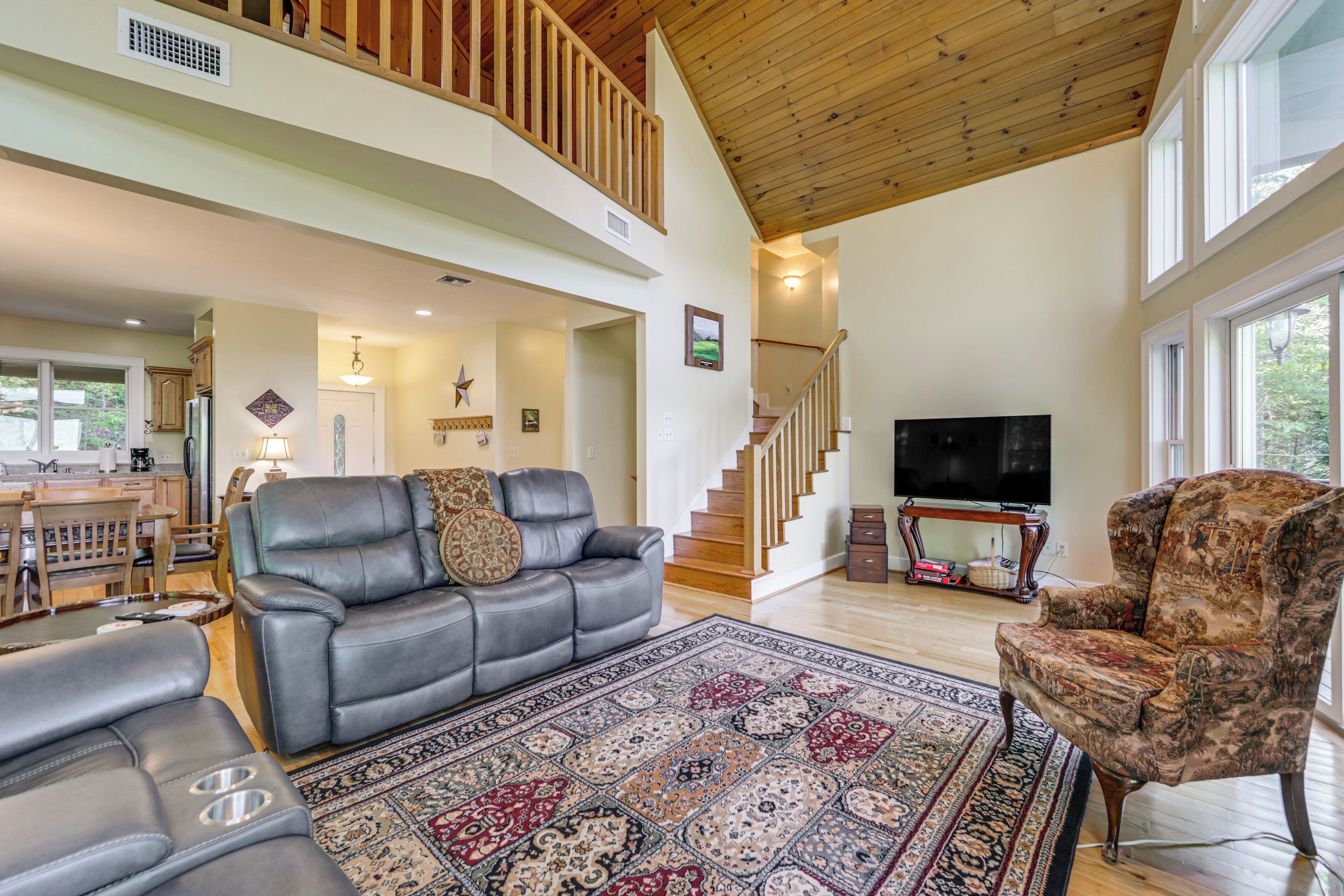 A spacious living area with a high ceiling, a staircase, a large rug, leather sofas, and a television.