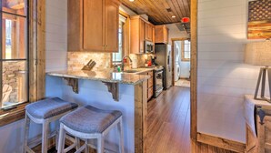 A kitchen with wooden cabinets, a granite countertop, and stainless steel appliances. There are two bar stools and a window with a view of the outdoors. - Pet-friendly Cabin w/ Mtn Views in Chinquapin! (Glenville)