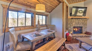 A cozy dining area with a wooden table set for two, a bench, and a fireplace with a stone surround. - Pet-friendly Cabin w/ Mtn Views in Chinquapin! (Glenville)