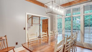 Un espace repas avec une table et des chaises en bois, de grandes fenêtres et un escalier menant à une autre pièce.