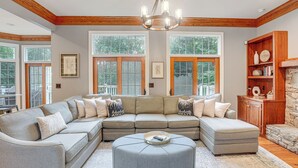 Un grand canapé d’angle en forme de L, doté de nombreux coussins, un pouf rond et un meuble en bois agrémenté d’objets décoratifs.