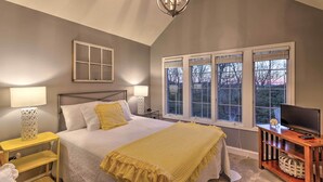 Une chambre à coucher avec un lit, des lampes de chevet, un téléviseur posé sur un meuble en bois et une fenêtre avec des stores.
