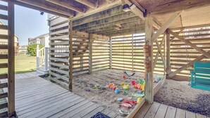 Une structure de jeu en bois avec un sol sablonneux et divers jouets.