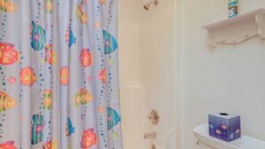 Une salle de bain avec un rideau de douche orné de motifs de poissons colorés, une baignoire blanche et une étagère sur laquelle se trouve une boîte de mouchoirs.