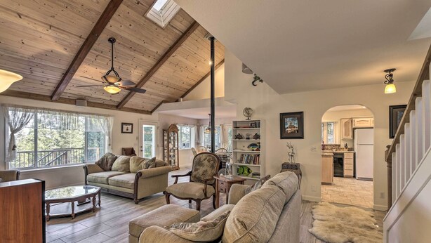 A spacious living room with a high ceiling, wooden beams, and a view of the kitchen through an archway. - 20 Mi to Lassen Park: Chateau w/ Mt Shasta View! (Shingletown)