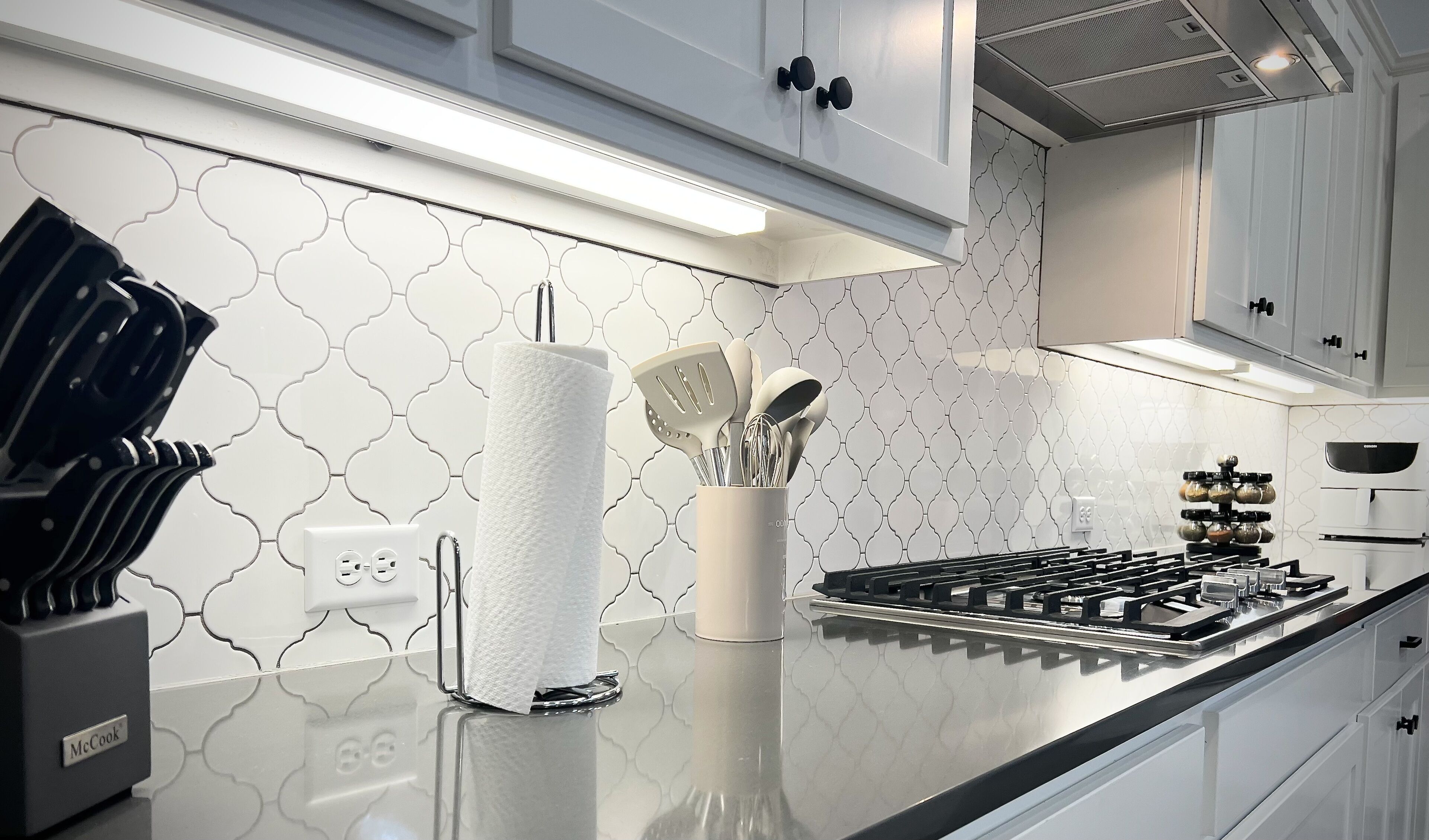 Una cocina moderna con armarios blancos, estufa de acero inoxidable y salpicadero con diseño geométrico.