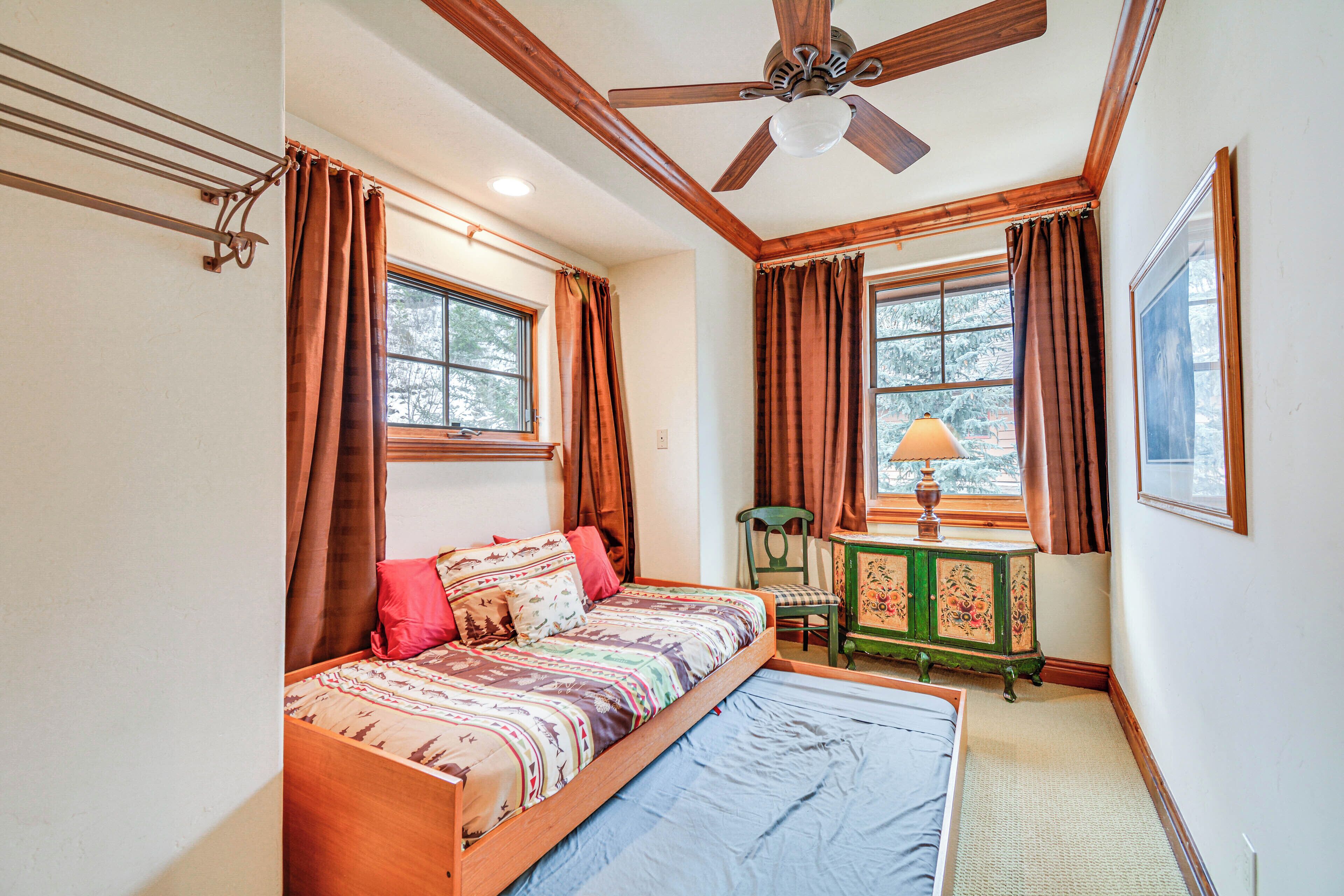 A bedroom with a bed, a desk with a lamp, and a ceiling fan.