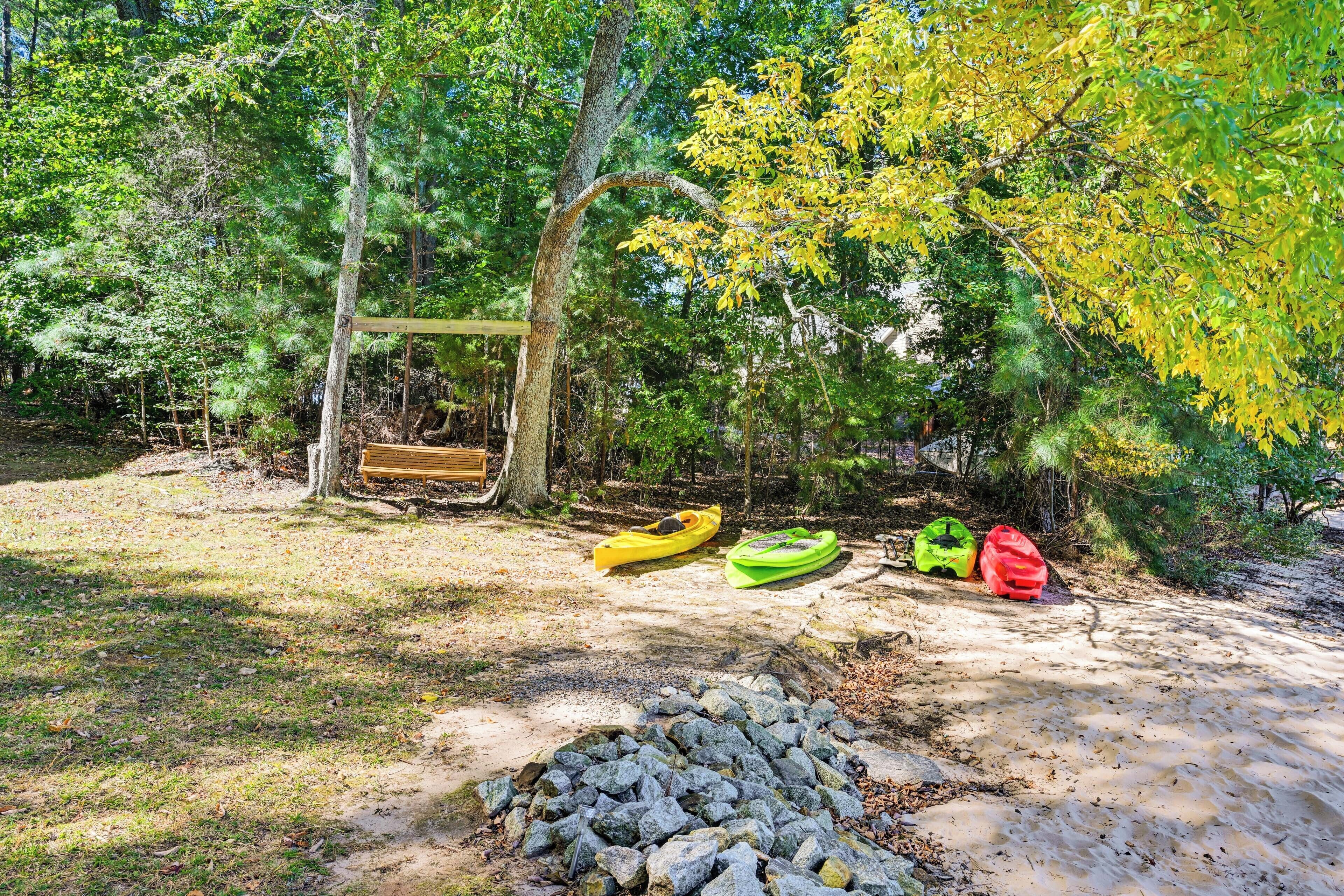 A forested area with a wooden bench, kayaks, and a pile of rocks.