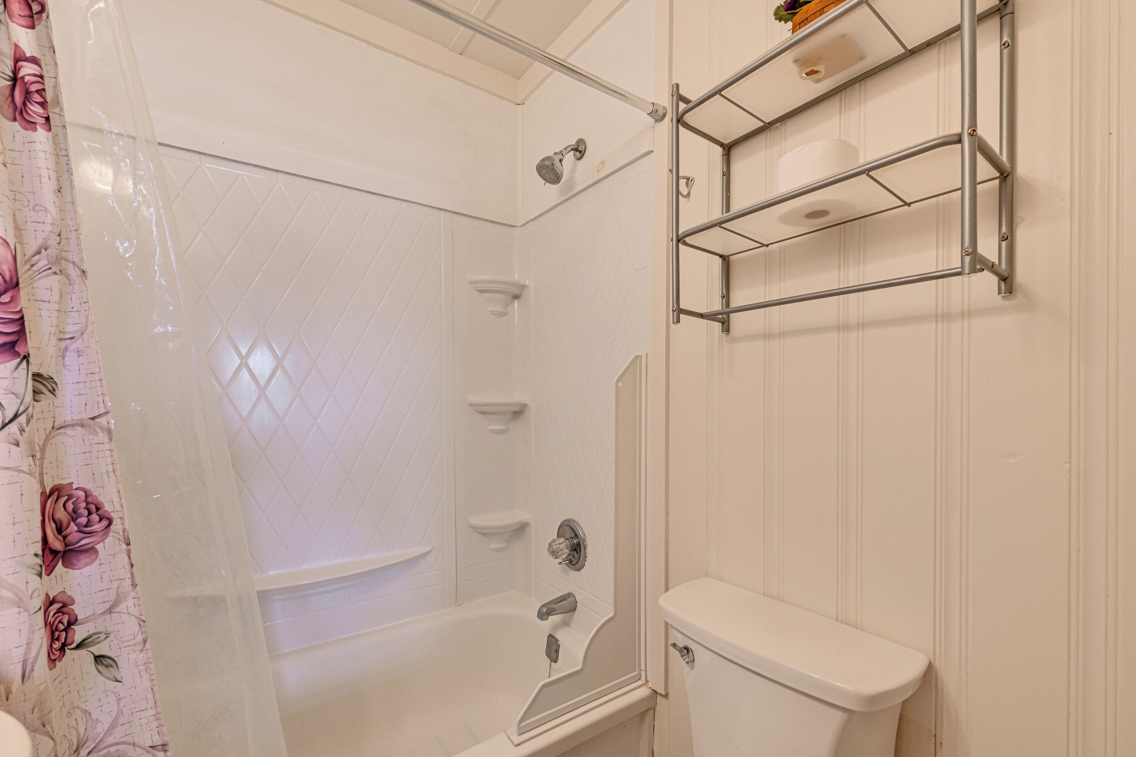 Un baño con ducha, inodoro y un estante con artículos de aseo.