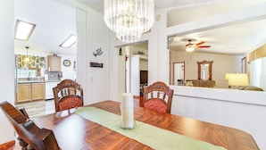 A dining area with a wooden table, chairs, a chandelier, and a view into the kitchen. - Mtn Gate Guest House ~ 6 Mi to Shasta Lake! (Redding)