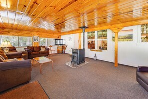 Una sala de estar acogedora con techos de madera, chimenea y grandes ventanas que ofrecen vistas del exterior.