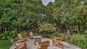 An outdoor patio with Adirondack chairs, a fire pit, and a stone table. - Airy Cottage Close to Rock Lake w/ Fire Pit! (Lake Mills)