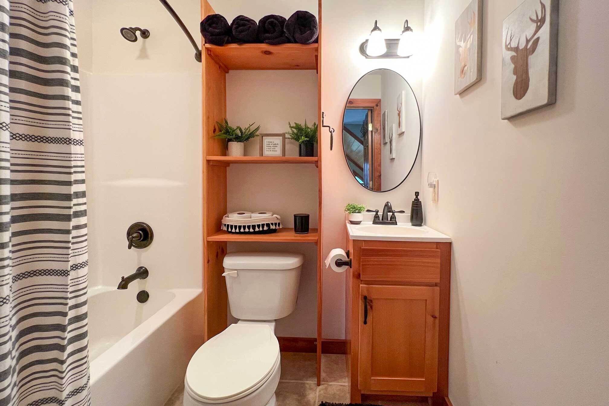 A compact bathroom with a toilet, sink, and shower. There are shelves with toiletries and a mirror above the sink.