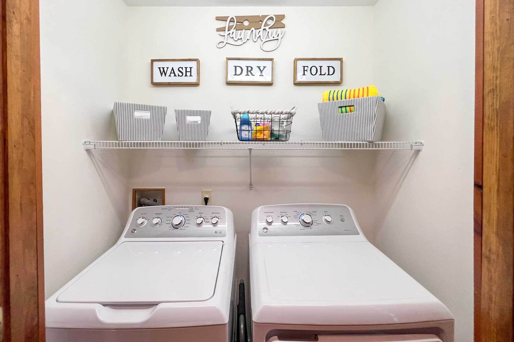 A laundry room with two washing machines, a drying rack, and a shelf with laundry supplies.