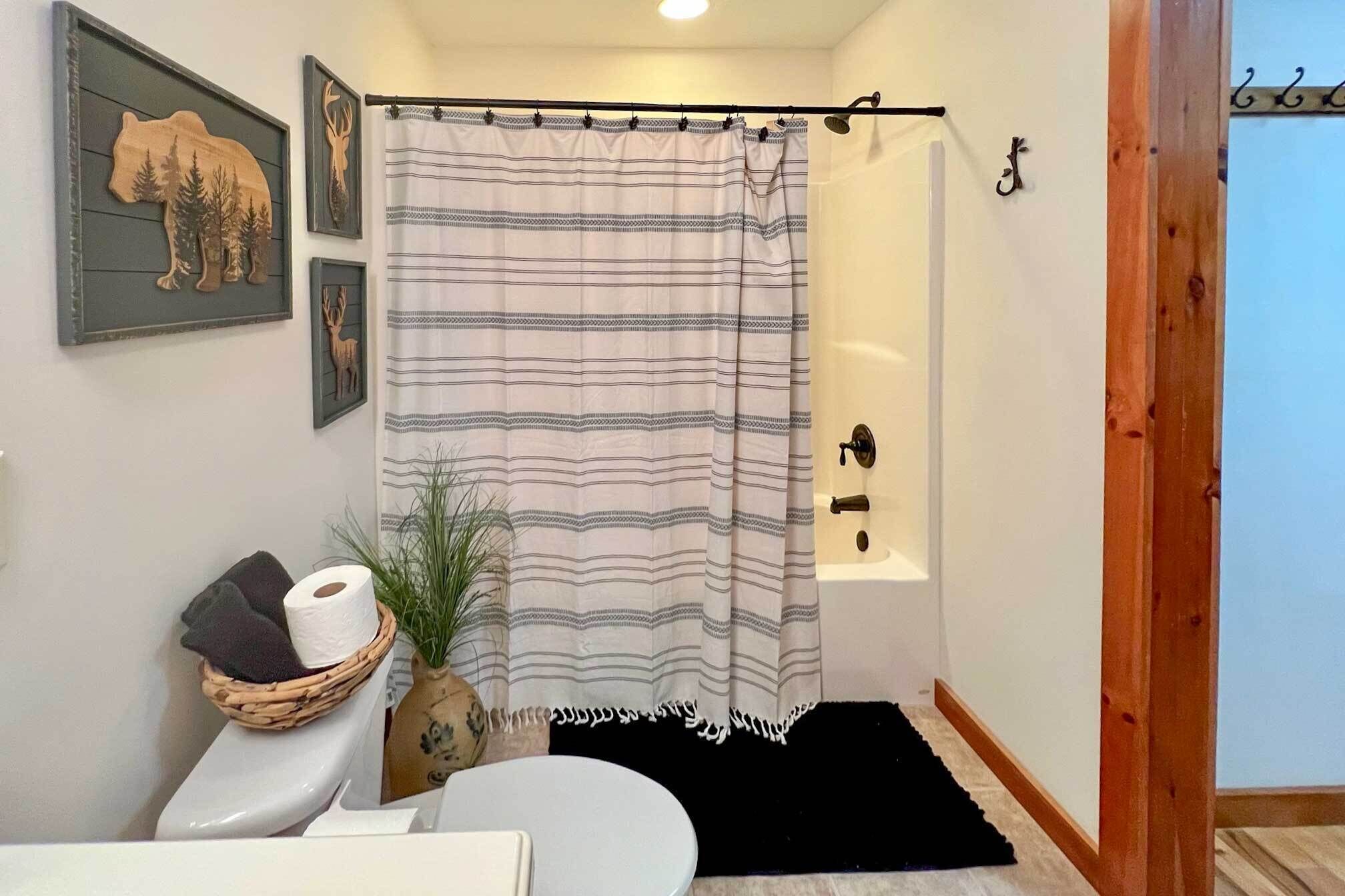 A bathroom with a striped shower curtain, a toilet, a sink, a decorative wall piece, and a small plant.