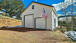 A single-story building with two garage doors, an American flag, and a wooden fence. - Colorado Vacation Rental w/ Deck & Mtn Views (Cripple Creek)