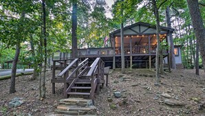A cabin with a wooden deck, stone steps, and an American flag. - Broken Bow Oasis: Hot Tub, Fire Pit & Patio (Broken Bow)