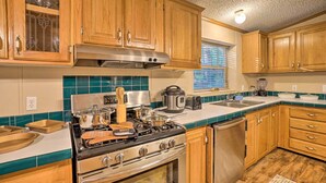 A kitchen with wooden cabinets, a stove, a dishwasher, and a window with blinds. - Broken Bow Oasis: Hot Tub, Fire Pit & Patio (Broken Bow)