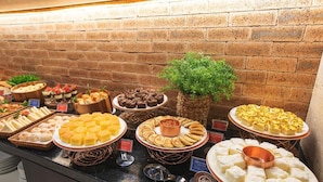 Un bufé con diversos alimentos dispuestos en fuentes y platos, incluyendo postres y pasteles, sobre un fondo de pared de ladrillo.