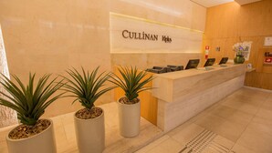 Un mostrador de recepción con un cartel que dice "CULLINAN Hotel". Hay tres plantas en macetas frente al mostrador.
