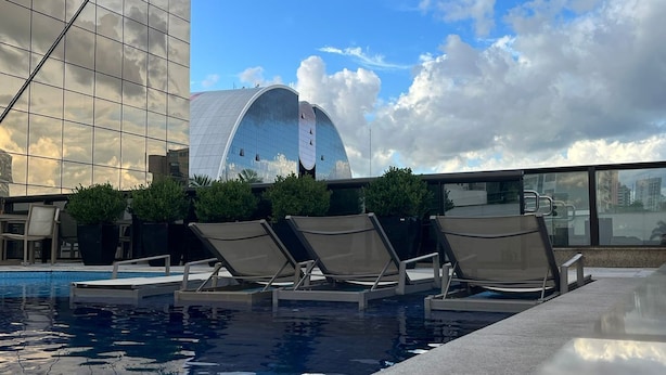 Una piscina con sillas de descanso, un edificio moderno con fachada de vidrio y una estructura en forma de cúpula al fondo.