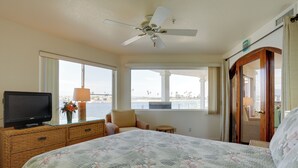 Une chambre à coucher avec un lit, un téléviseur posé sur une commode, une fenêtre donnant sur un paysage agréable et un ventilateur de plafond.