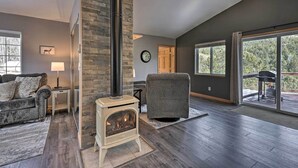 Un salon doté d’une cheminée en pierre, d’un canapé, d’un fauteuil et d’une grande fenêtre donnant sur l’extérieur.