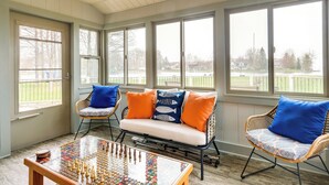 A sunroom with a sofa, two chairs, a coffee table, and large windows overlooking a yard. - Cadillac Vacation Rental w/ Dock on Lake Mitchell! (Cadillac)
