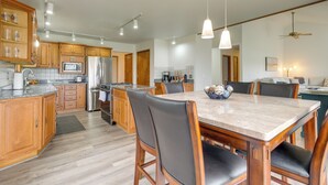 A modern kitchen with wooden cabinets, a granite countertop, stainless steel appliances, and a dining area with a marble table and leather chairs. - Cadillac Vacation Rental w/ Dock on Lake Mitchell! (Cadillac)