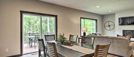 A spacious living area with a dining table, chairs, and a sofa. There is a fireplace and a television mounted on the wall.