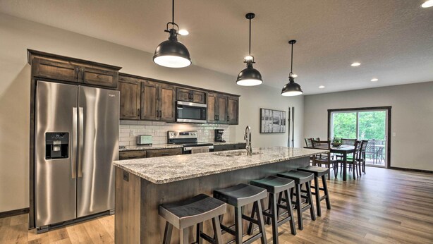 A modern kitchen with stainless steel appliances, a large island with bar stools, and pendant lighting. - Upscale Townhome in Causeways on Gull Resort! (Nisswa)