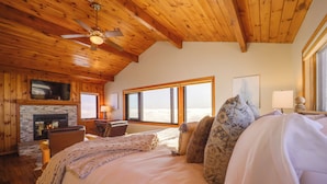 A cozy bedroom with a large bed, a fireplace, a television, and a view of the outdoors. - Views & Hot Tub! Beech Mtn 'sky Barn Retreat' (Banner Elk)