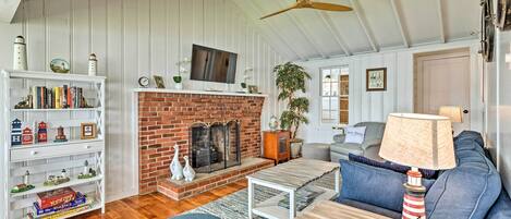 A cozy living room with a brick fireplace, white wooden walls, a bookshelf, and a blue sofa.