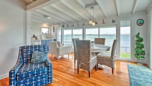 A spacious living area with a view of the ocean, featuring a dining table, chairs, and a blue armchair with anchor patterns. - Waterfront Portsmouth Cottage: 8 Mi. From Newport! (Portsmouth)
