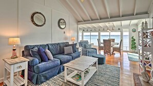 A living room with a blue sofa, white coffee table, and a view of the ocean through large windows. - Waterfront Portsmouth Cottage: 8 Mi. From Newport! (Portsmouth)
