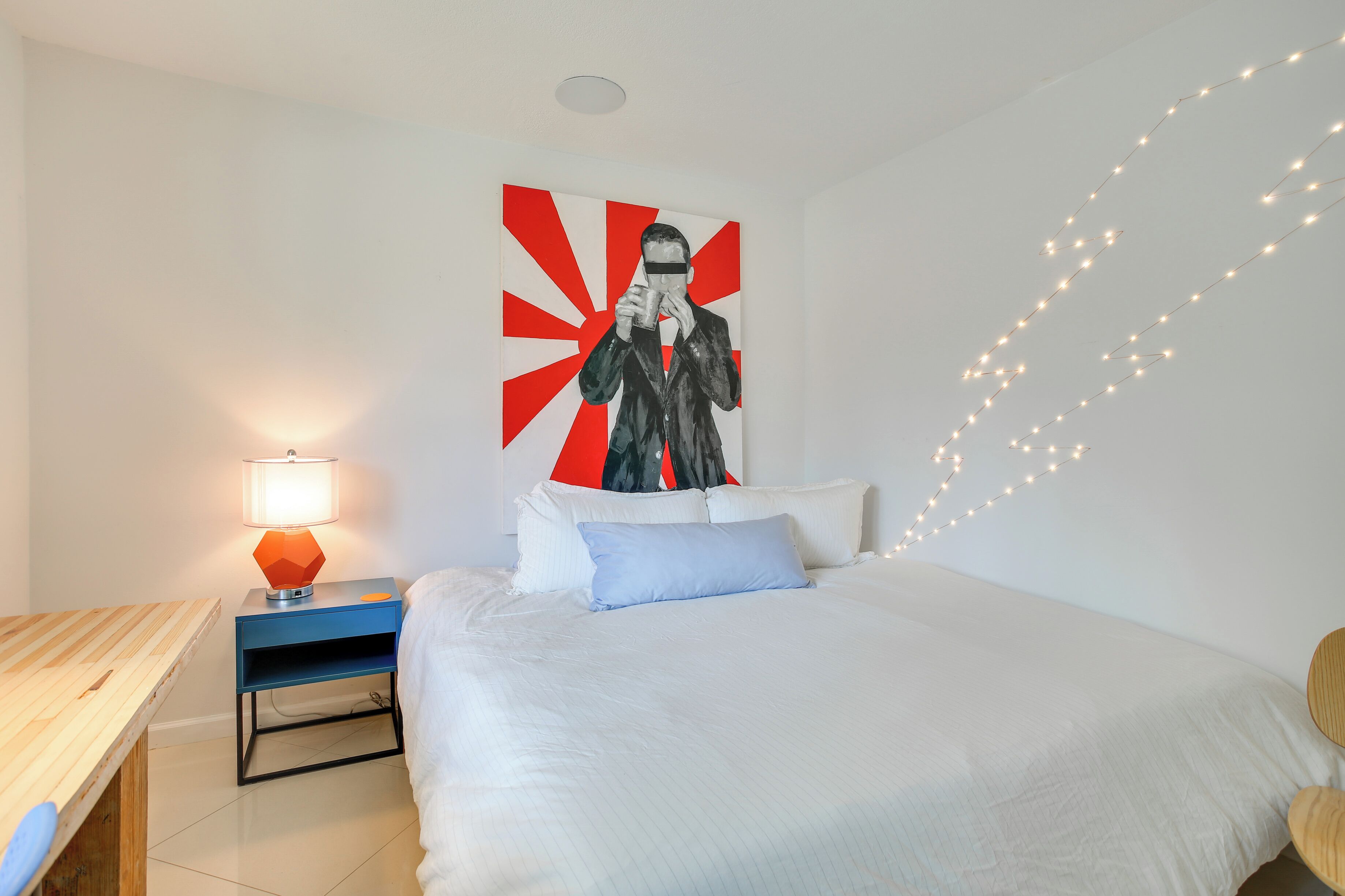 Ein Schlafzimmer mit einem Bett, einem Nachttisch mit Lampe, einem Bild an der Wand und Lichterketten.