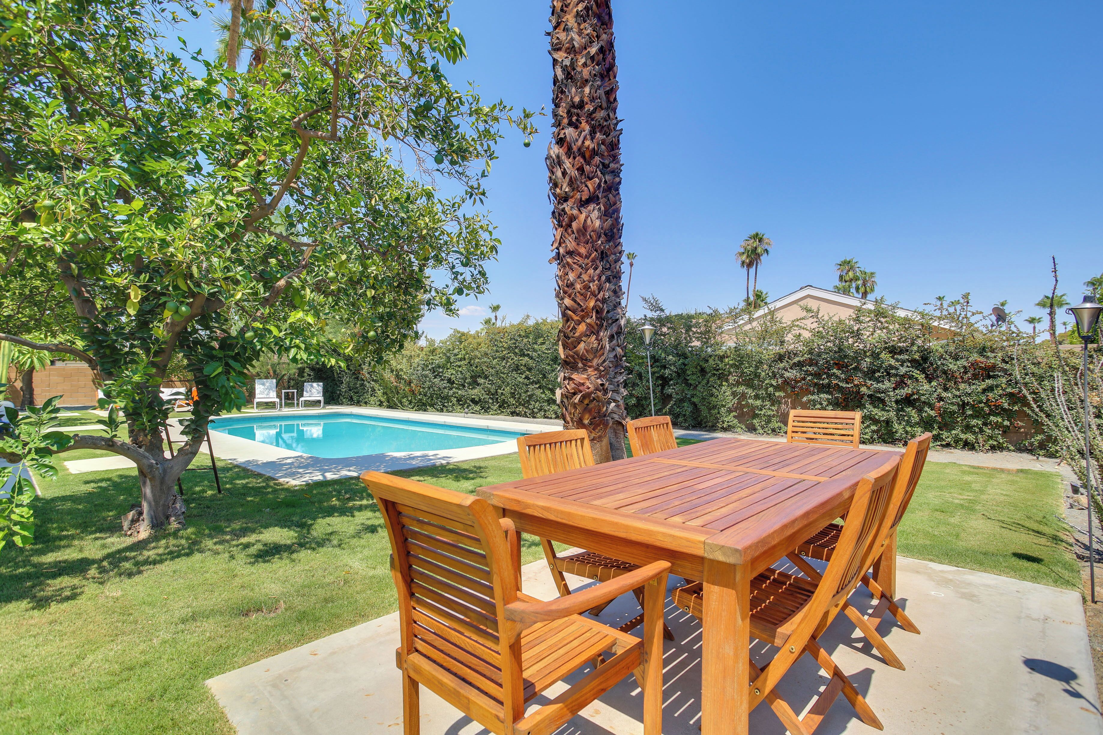 Une table et des chaises en bois sur une terrasse, avec une piscine en arrière-plan.