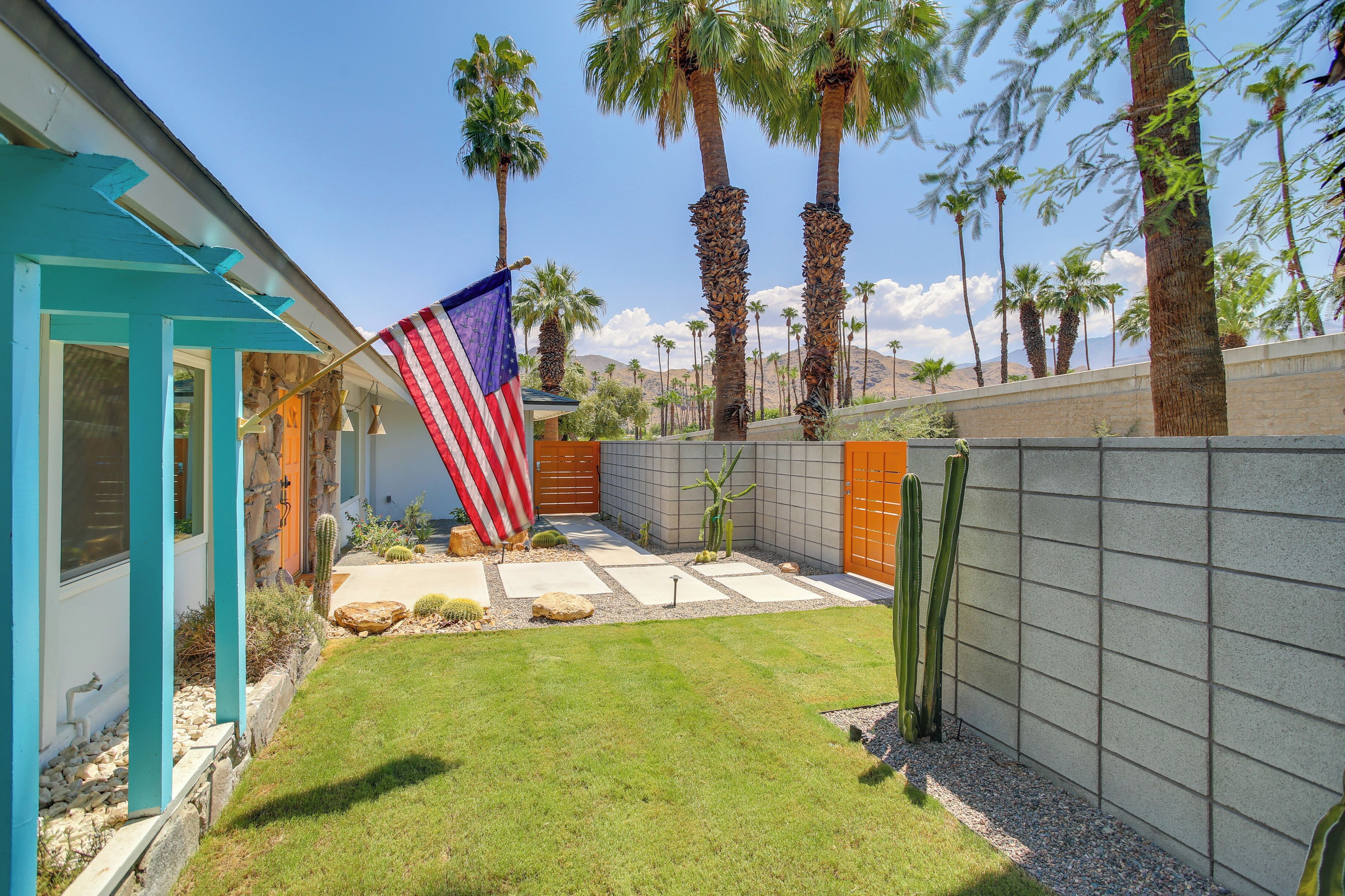 A residential property with a well-maintained lawn, a patio area with a flag, and a variety of cacti and other desert plants.