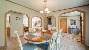 A dining area with a wooden table and white chairs, a chandelier, and a view into the kitchen. - Secluded Ohio Getaway on 65 Acres! (Andover)
