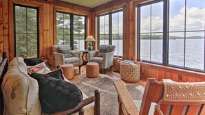 A cozy cabin interior with large windows overlooking a lake, furnished with a sofa, chairs, and a small table. - Waterfront Star Lake Cabin, Boat Dock On-site (Star Lake)