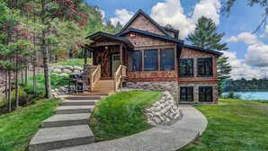 A two-story log cabin with a stone foundation, a wooden deck, and a stone retaining wall. - Waterfront Star Lake Cabin, Boat Dock On-site (Star Lake)