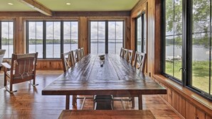 A wooden dining table with chairs, large windows, and a view of a lake. - Waterfront Star Lake Cabin, Boat Dock On-site (Star Lake)