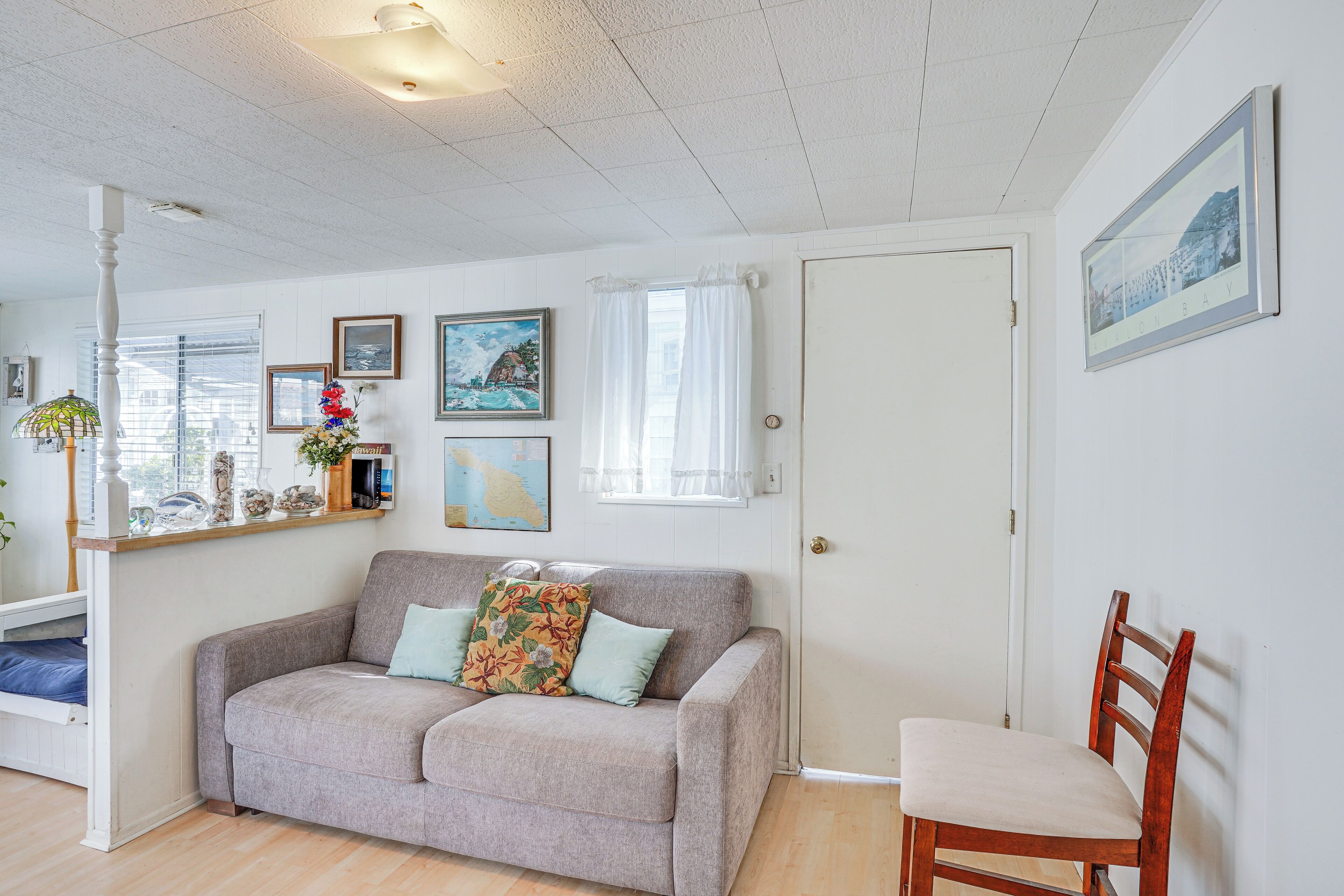 A living room with a grey sofa, a wooden chair, a white door, and a window with curtains.
