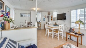 A spacious room with a wooden dining table, white chairs, a television, and a window with blinds. - Quaint Avalon Cottage < Half-mi to Beaches! (Avalon)